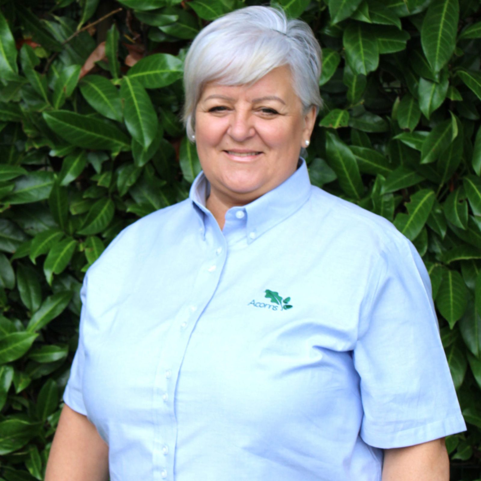 Acorns Nurseries A person in a light blue shirt stands gracefully in front of a leafy green background at Acorns Duffryn.