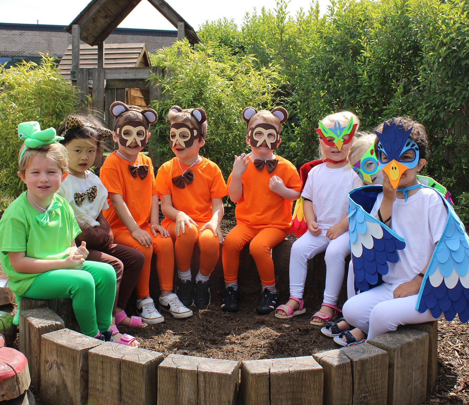 Acorns Nurseries Children in animal costumes sit together outdoors on wooden benches, surrounded by greenery at Parc Nantgarw on a sunny day, eagerly collecting acorns.