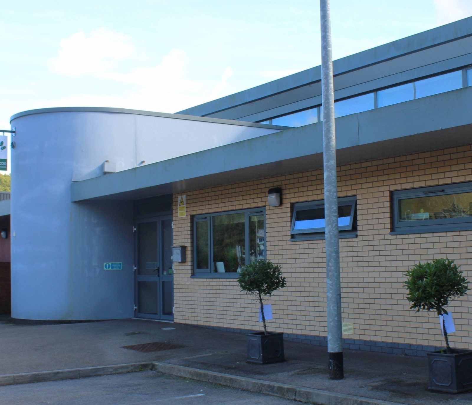 Acorns Nurseries A modern building with beige brickwork and a curved entrance, nestled in Nantgarw. Small trees in pots greet visitors near the doorway, adding charm to this Parc Nantgarw haven.