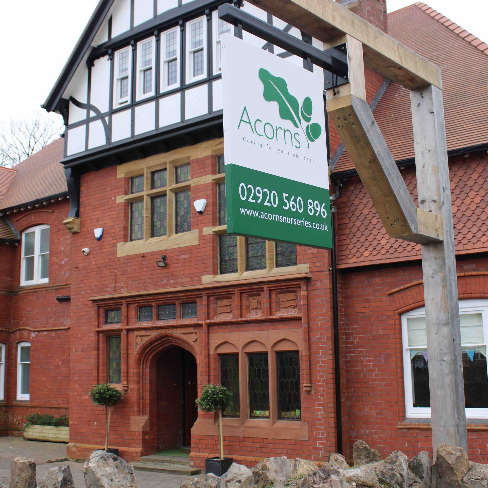 Acorns Nurseries A brick building with a Tudor-style facade and a sign reading "Acorns" stands prominently in Llandaff. It features a stone fence, adding to its classic charm, with a phone number displayed for contact.