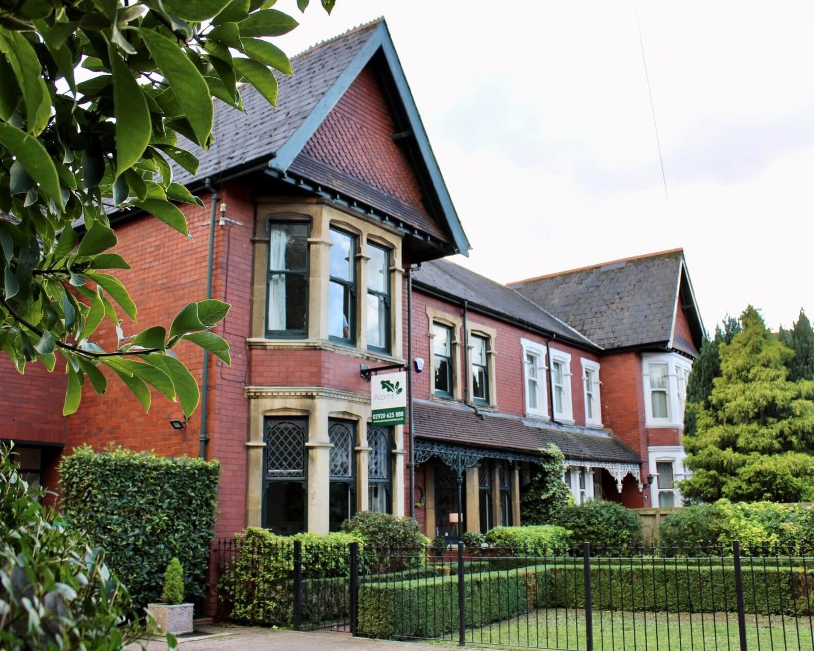 Acorns Nurseries A row of Victorian-style brick houses in Whitchurch boasts large windows, ornate details, and a tidy front garden with acorns scattered behind a black fence.