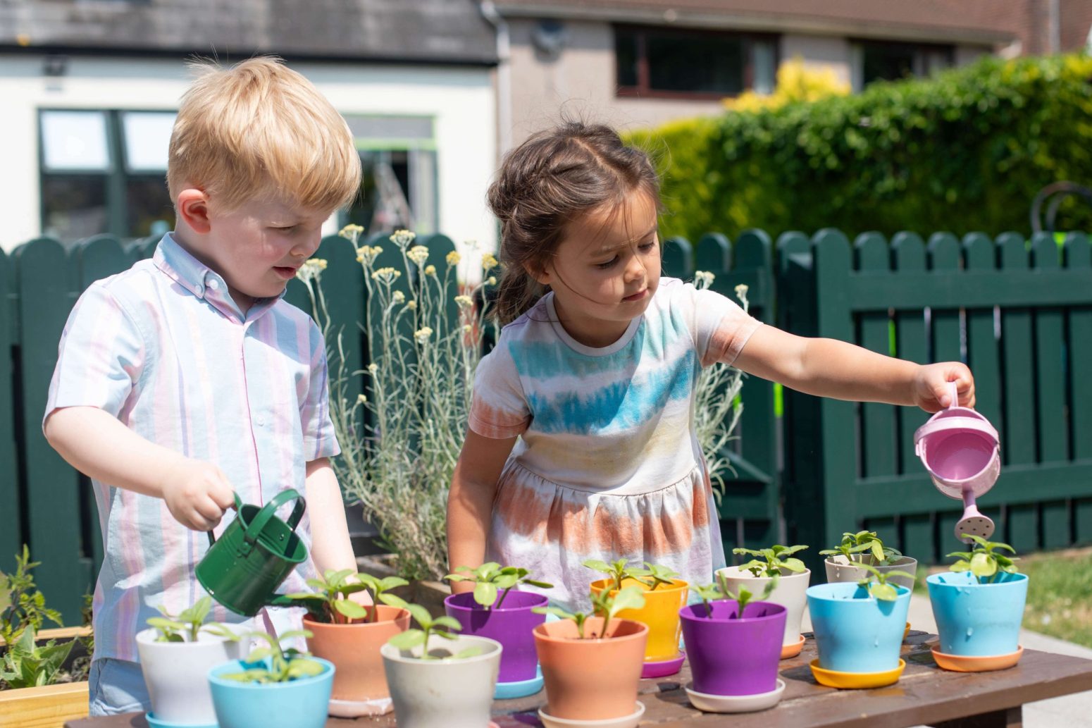 Acorns Nurseries Two children are outside in their home garden, joyfully using small watering cans to hydrate the potted plants.