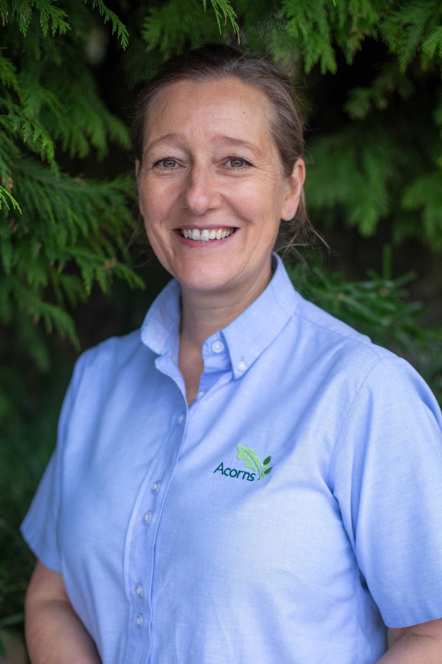 Acorns Nurseries Person smiling outside, wearing a light blue shirt with an 